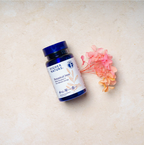 Vitamin supplement bottle labeled 'Higher Nature' on a light surface with flowers.